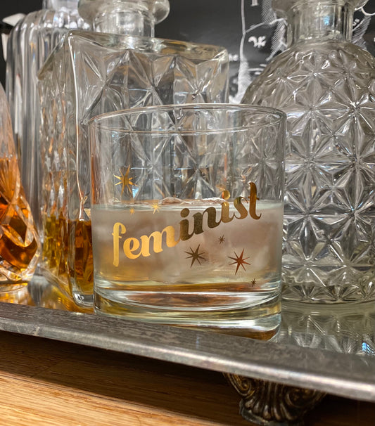 drinking glass that has feminist and stars printed on it in gold